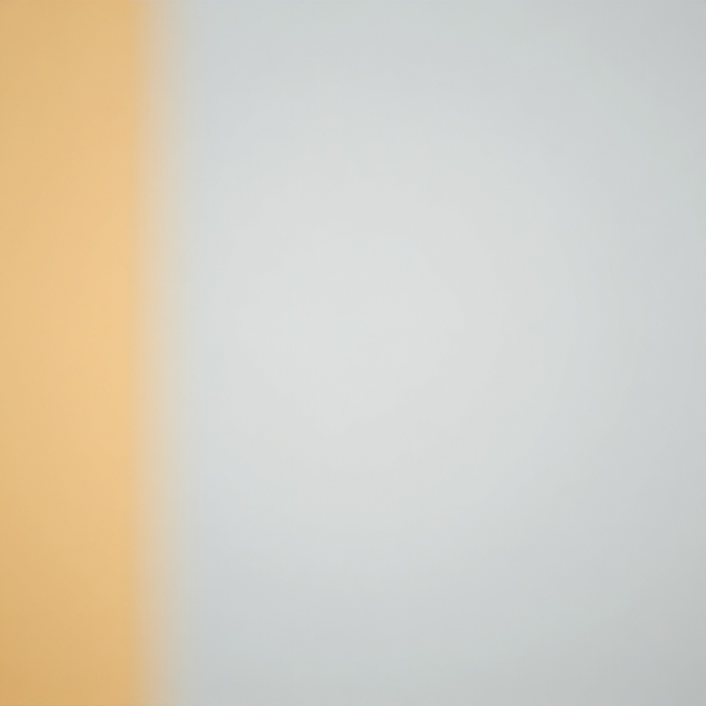 The image is a blurred, out-of-focus background consisting of a vertical, muted yellow-orange stripe on the left side, contrasted against a soft, pale gray field. The composition has a minimalist and abstract aesthetic, suggesting a smooth, solid surface with diffused lighting. The overall mood is calm, neutral, and unobtrusive.